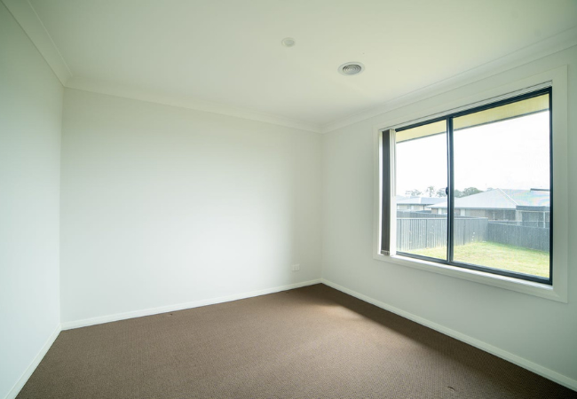 Empty room with brown carpet, white walls, and a window overlooking a grassy area.