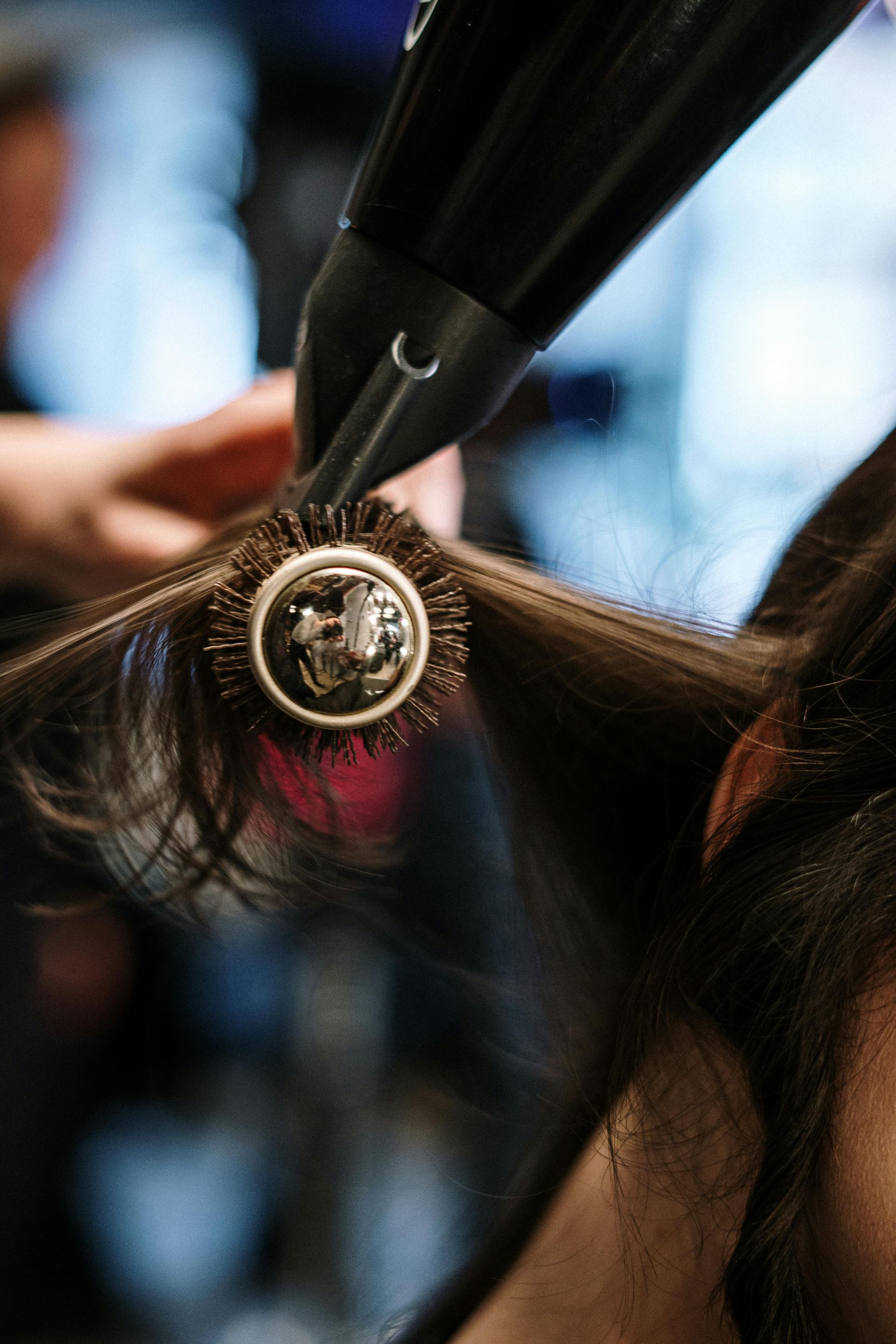 Hair being styled with a round brush and hairdryer at a close range, indoors.