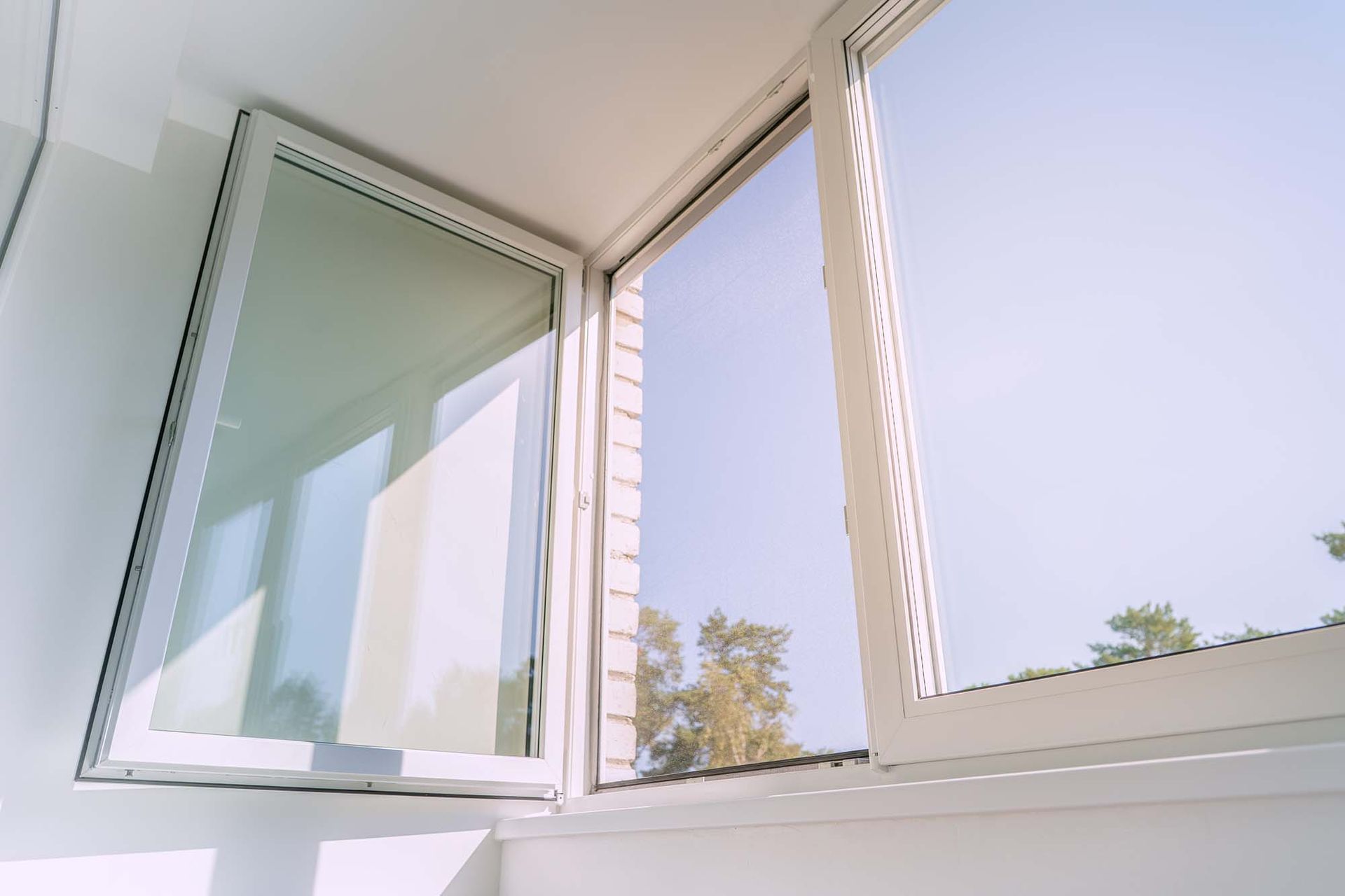 Open white window with a view of trees and blue sky, letting bright daylight into a room