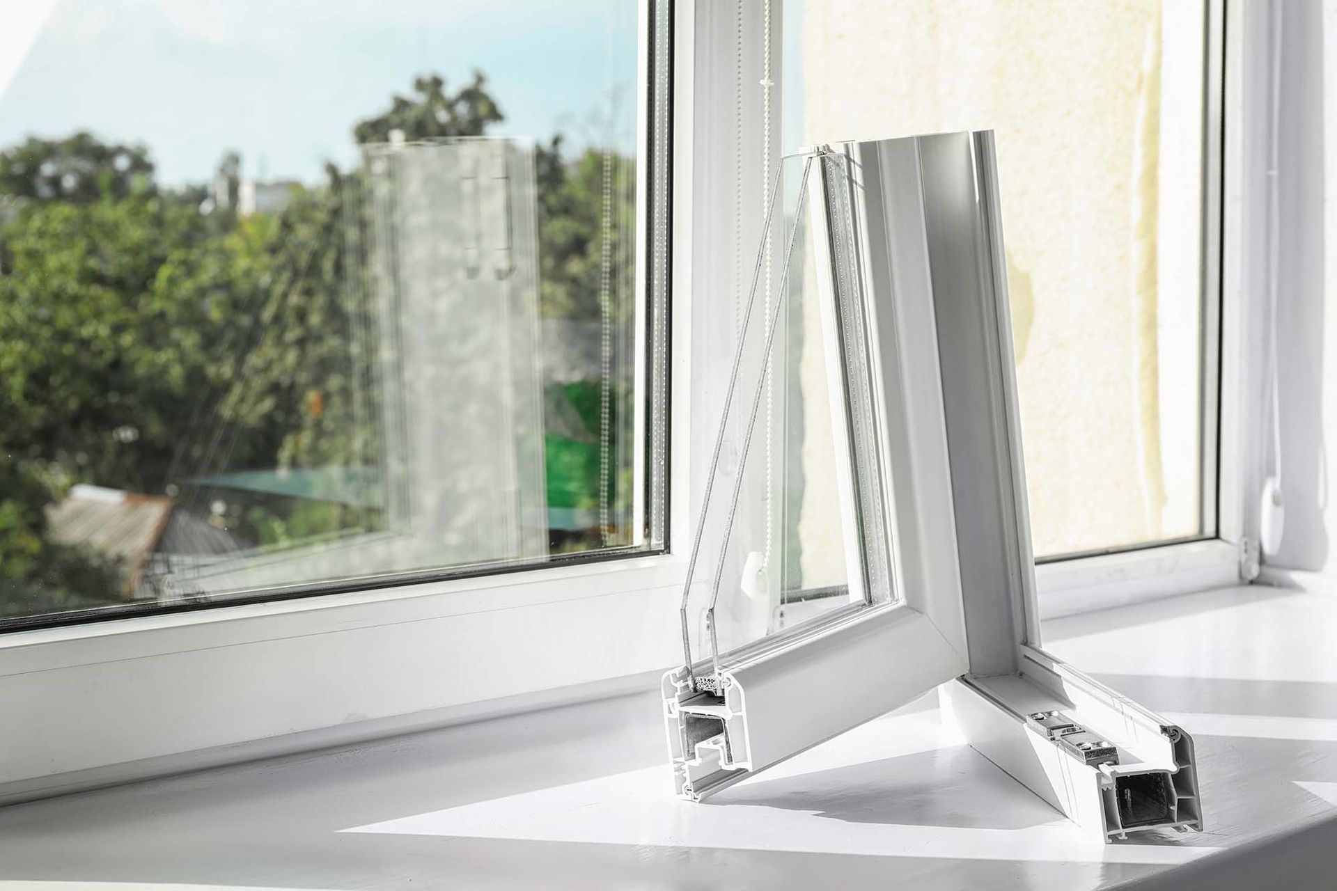 Open white window propped open on a sunny windowsill with trees outside