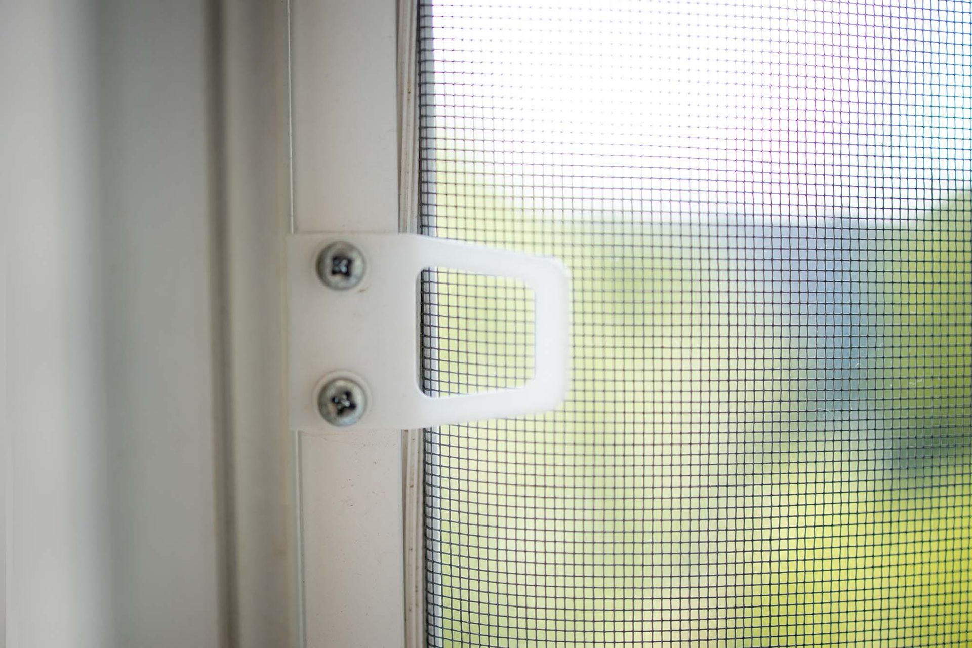 White window latch on a screened window with daylight outside