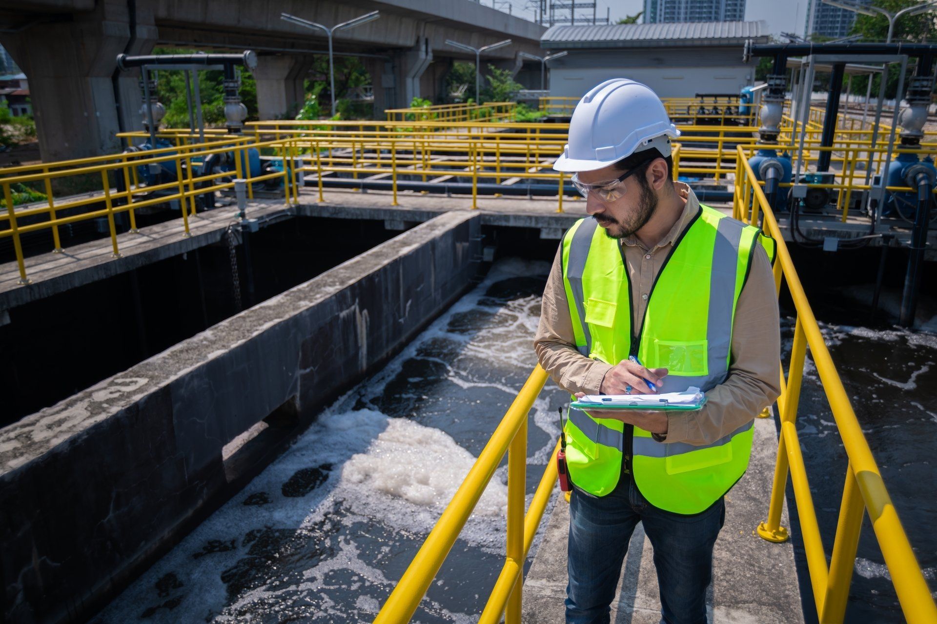 Engineer in white hard hat and neon vest taking notes at a wastewater treatment plant