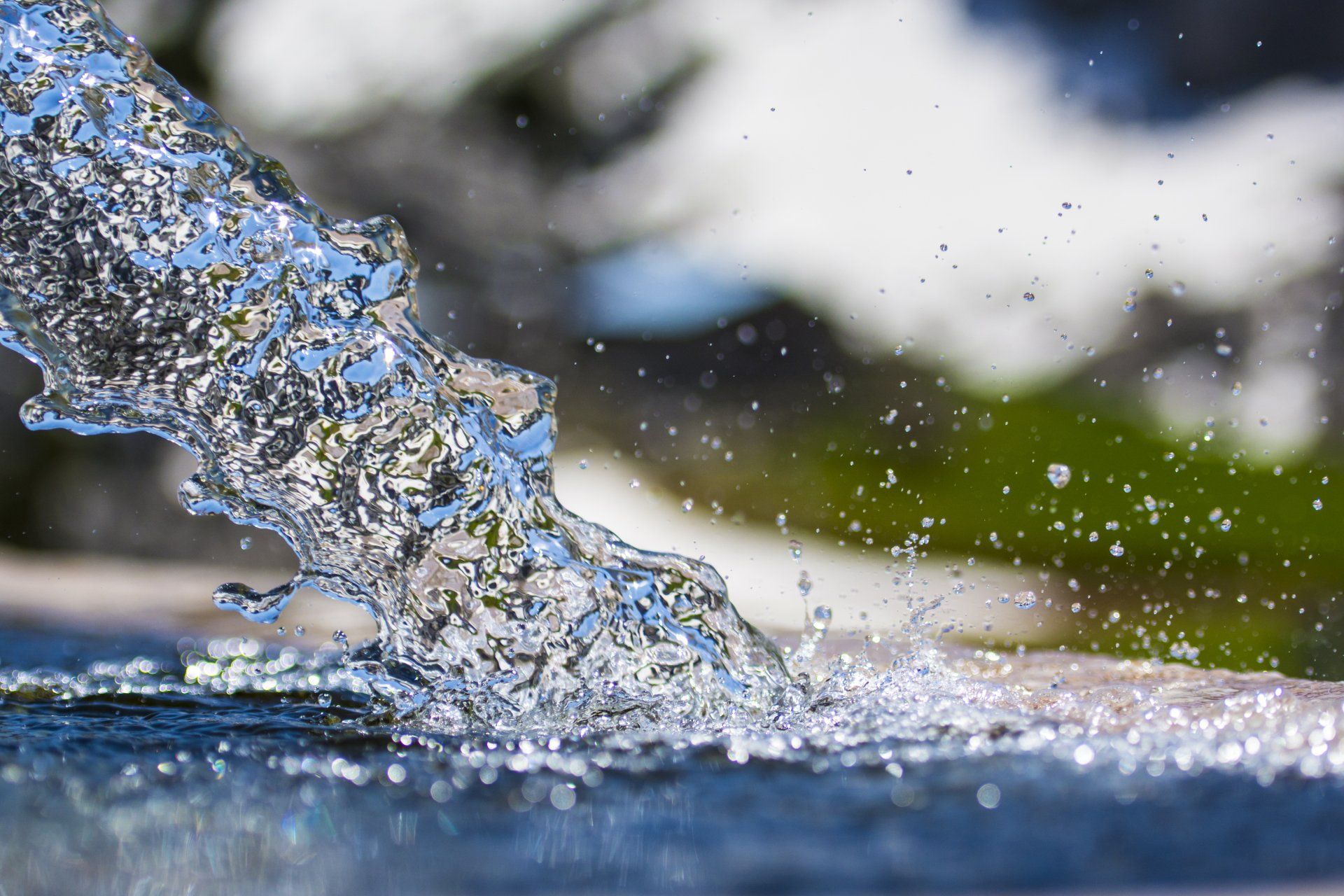 Clear water splashing over a dark surface, with droplets spraying against a blurred outdoor background