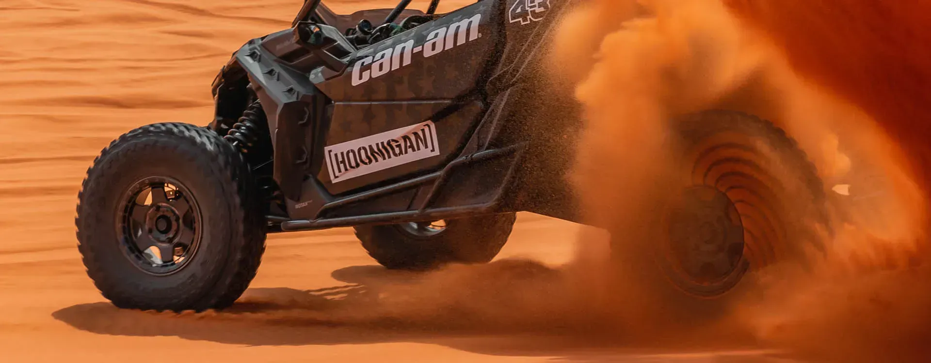 a can-am atv is driving through the sand on a dirt road .