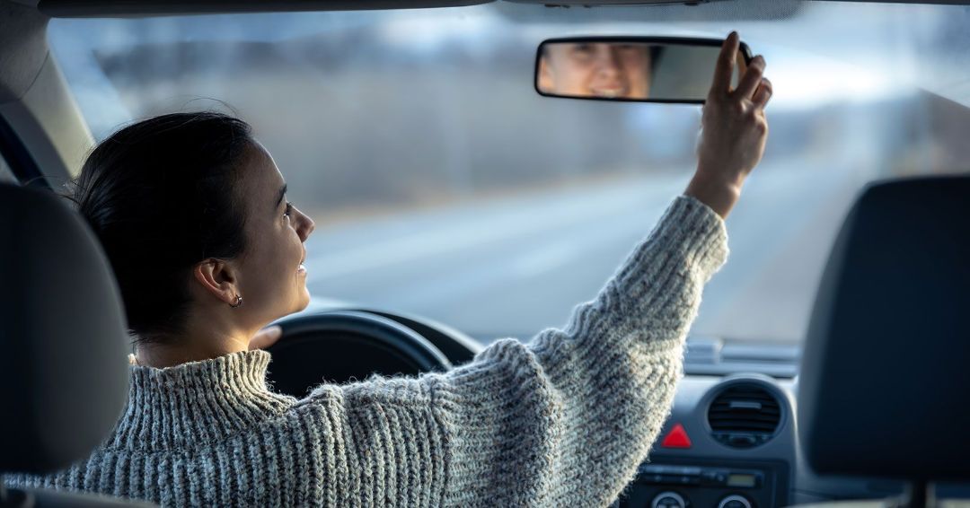 a woman is taking a selfie in the rear view mirror of her car .