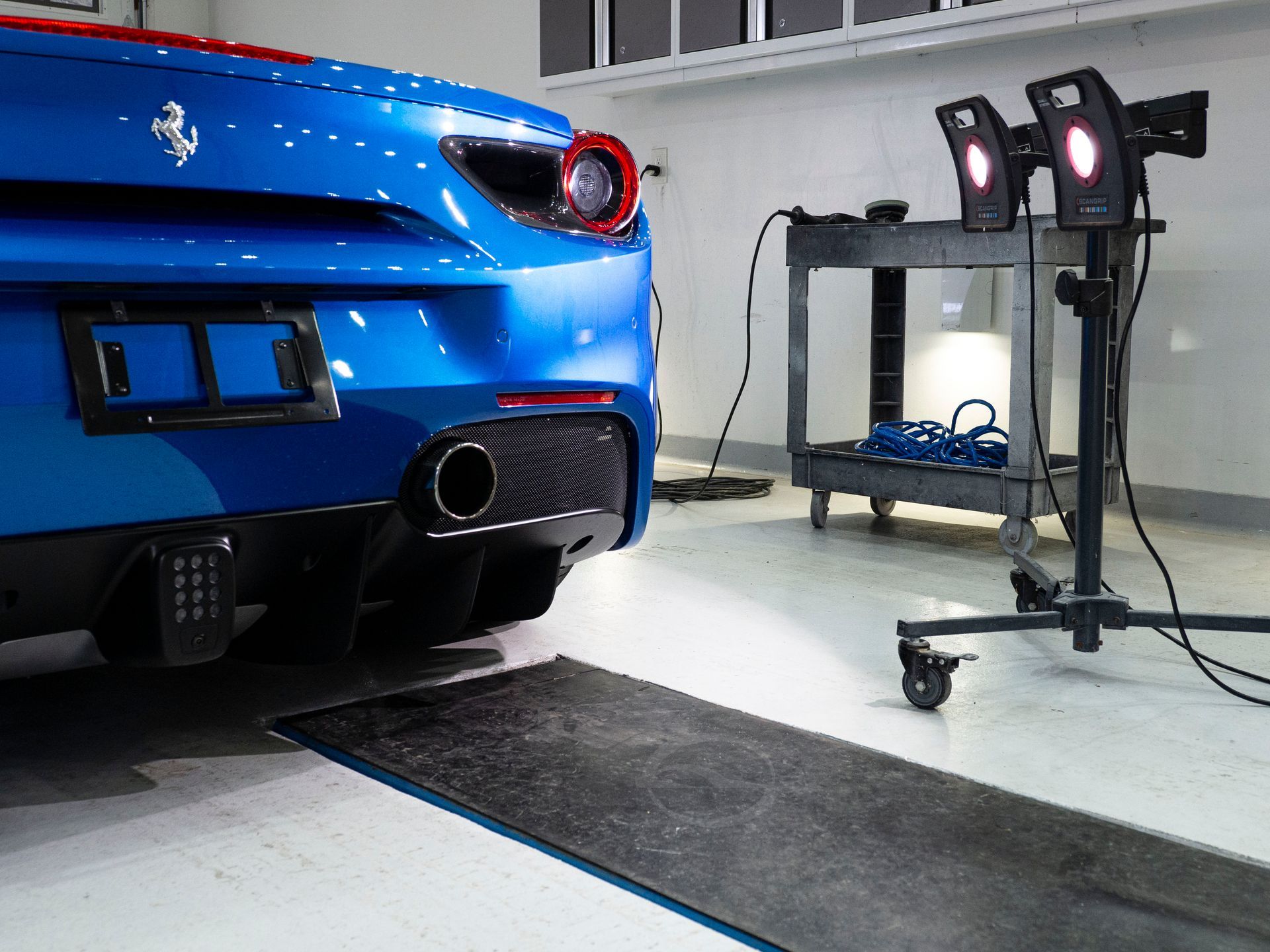 A blue ferrari is parked in a garage next to a light stand