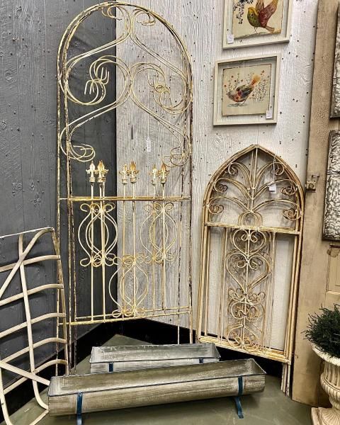 Decorative white metal arch and gate panels displayed in a shop, with framed art on the wall.