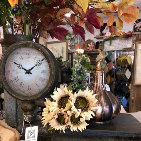 Vintage tabletop display with rustic clock, metal vase, and sunflower arrangement