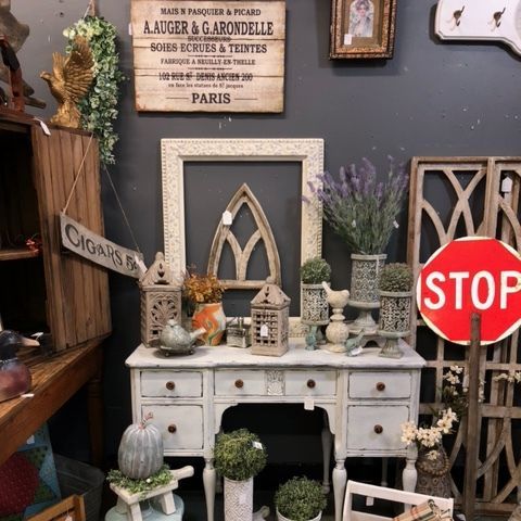 Vintage display with white desk, decorative arches, plants, and a red STOP sign against a dark wall