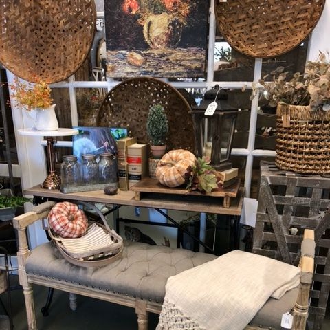 Cozy vintage tabletop display with baskets, pumpkins, jars, and a cushioned bench with folded blankets