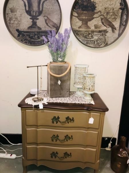Decorative wooden dresser with flowers, trays, and wall art in a corner against a white wall