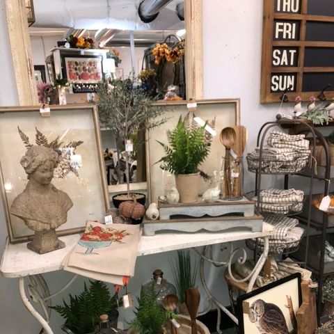 Vintage decor display with framed art, bust sculpture, plants, and woven baskets in a shop interior