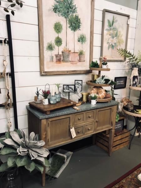 Rustic home decor display with wooden cabinet, framed wall art, and potted plants
