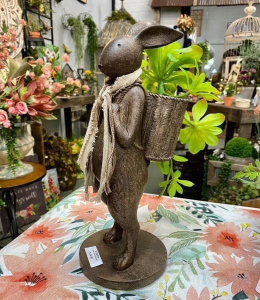 Decorative rabbit figurine with a basket, standing on a floral tablecloth in a plant shop