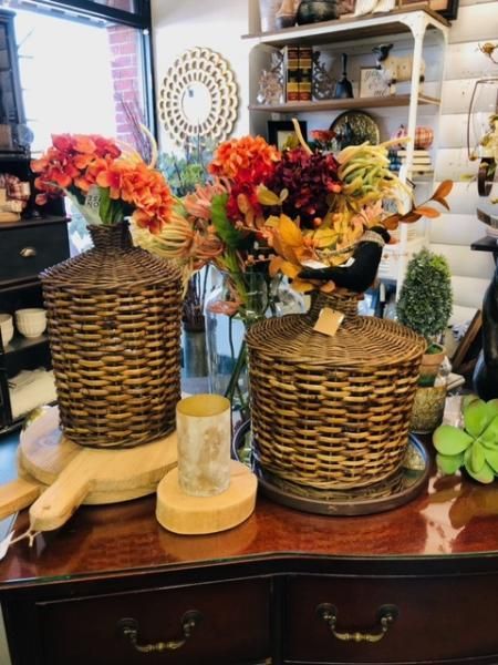 Two woven vases with colorful artificial flowers on a wooden dresser in a home decor shop