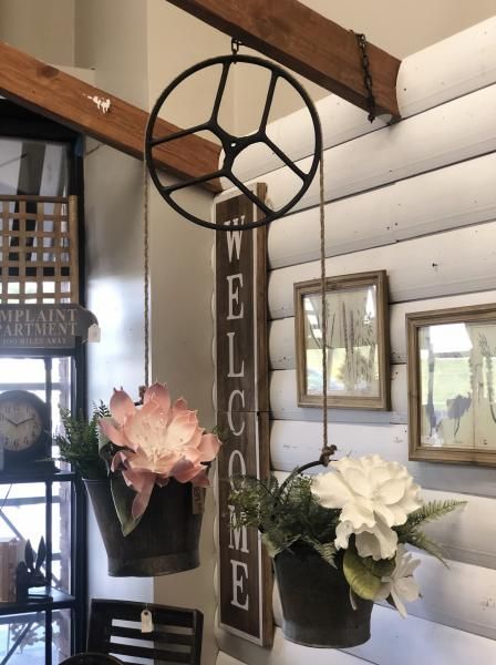 Rustic porch decor with a “WELCOME” sign and two hanging flower baskets under wooden beams.