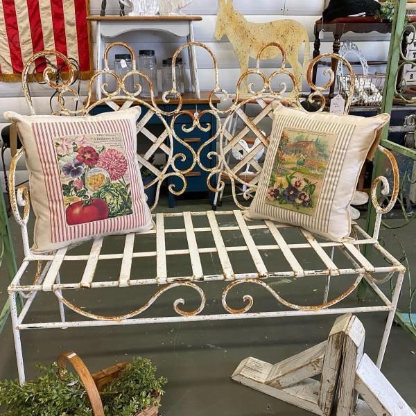 White wrought-iron bench with floral cushions and gold decorative garden chairs in a shop display