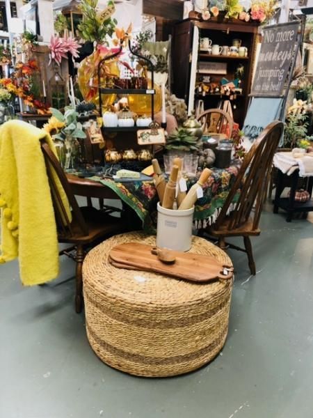 Decorated boho table display with woven ottoman, yellow chair drape, plants, and candles in a shop interior