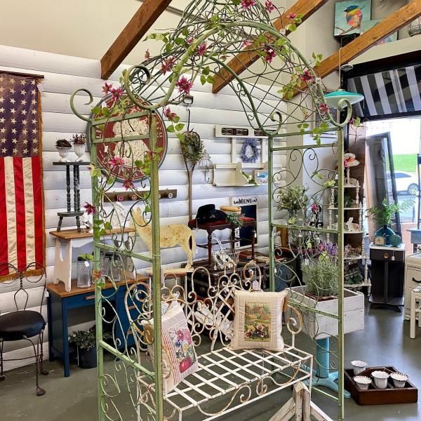 Decorative metal garden bench under an arched trellis in a bright shop display with flowers and pillows