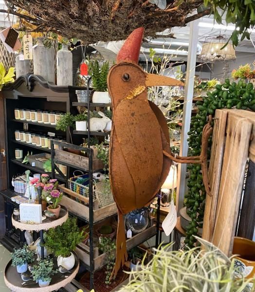 Rustic bird sculpture in a garden shop, with a red cone hat and wooden body