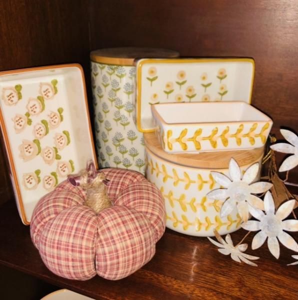 Decorative ceramic containers and a plaid fabric pumpkin arranged with white daisies on a wooden shelf
