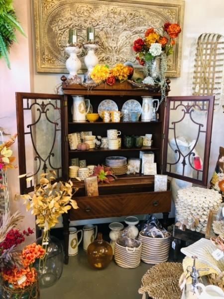 Decorative cabinet with shelves of dishes and flowers, flanked by metal side panels in a cozy room.