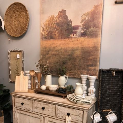 Rustic entryway console with woven decor, candles, white pitchers, and a large landscape print above.