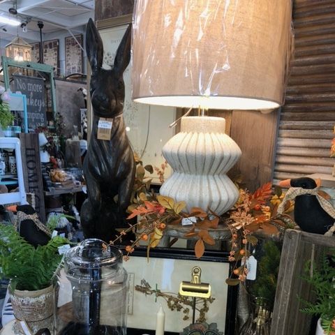 Decorative lamp and black rabbit statue displayed in a cozy shop window with plants and autumn accents