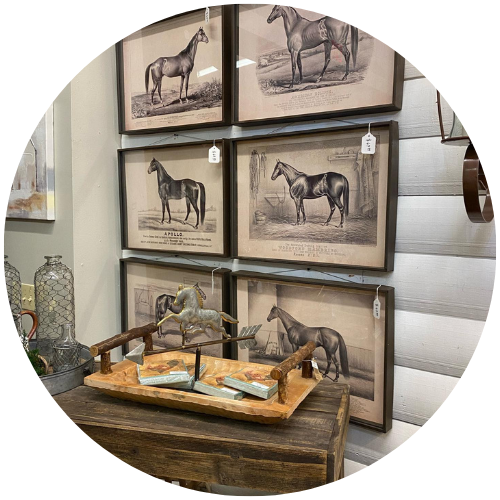 Framed horse prints on a wall above a wooden table with a tray and decorative items