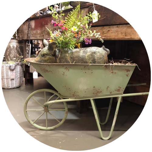 Vintage green wheelbarrow planter with colorful flowers and mossy rocks in an indoor display