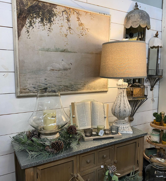 Decorative sideboard with lamp, open book, candles, greenery, and framed artwork in a cozy room