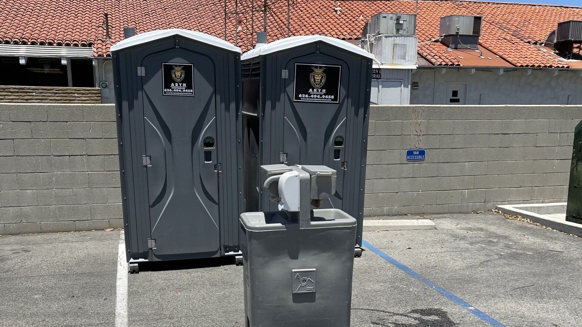 Two portable toilets and a hand washing station of Aryh Industries in a parking lot.