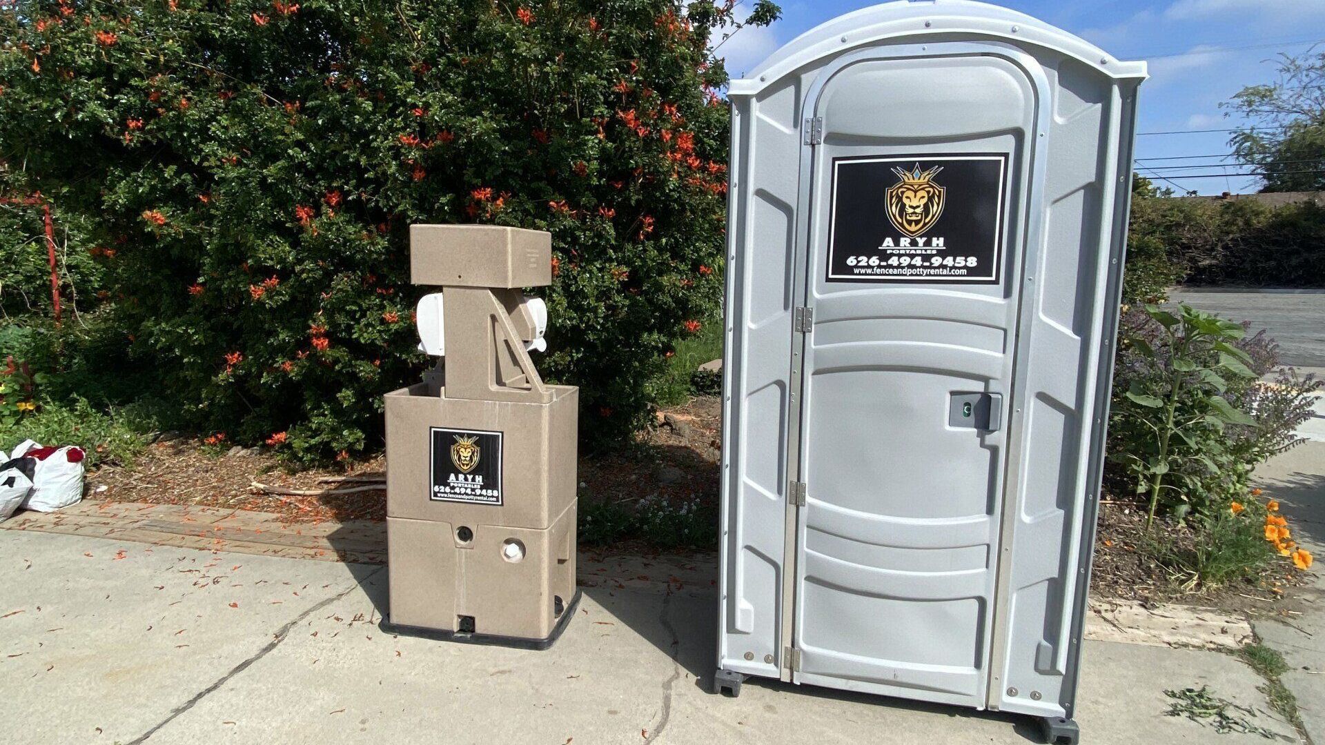 An Aryh portable toilet is next to a hand sanitizer station.