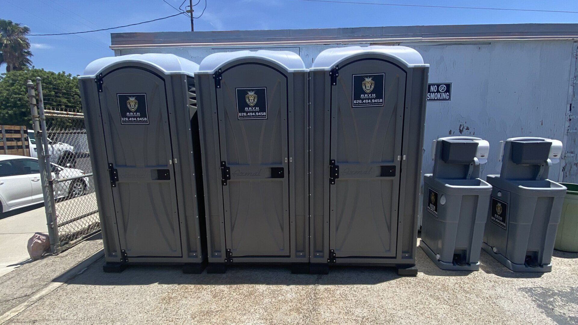 A row of Aryh's portable toilets sitting next to each other in a parking lot.