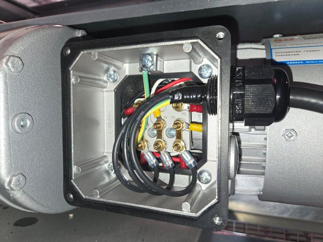 Close-up of an open electrical junction box with multicolored wires and terminal screws mounted on machinery.