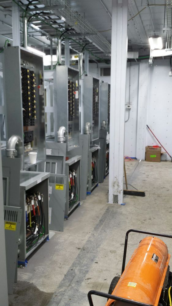 Industrial equipment in a factory aisle, with tall metal machines and an orange cylinder on the floor.