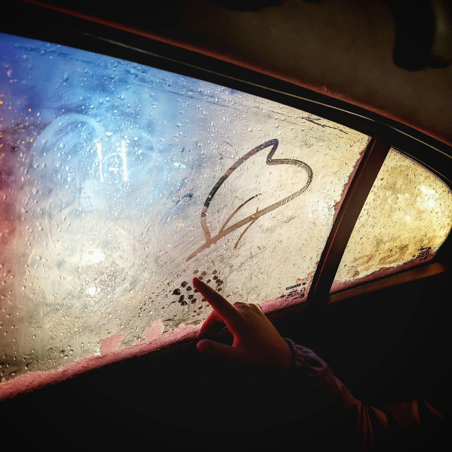 A person is pointing at a heart drawn on a car window