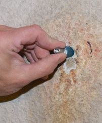 Hand scraping off a blue sticker from a beige countertop with a small tool