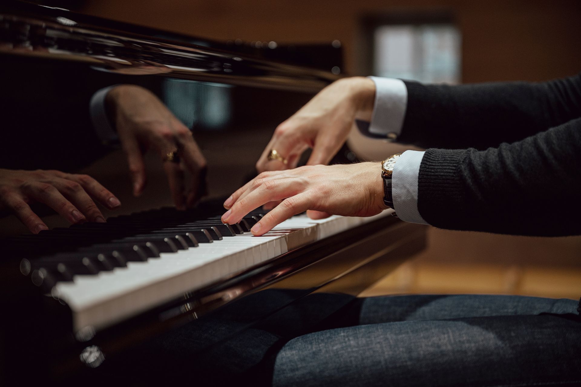 Hands playing a piano, with a reflective black surface and bench in view