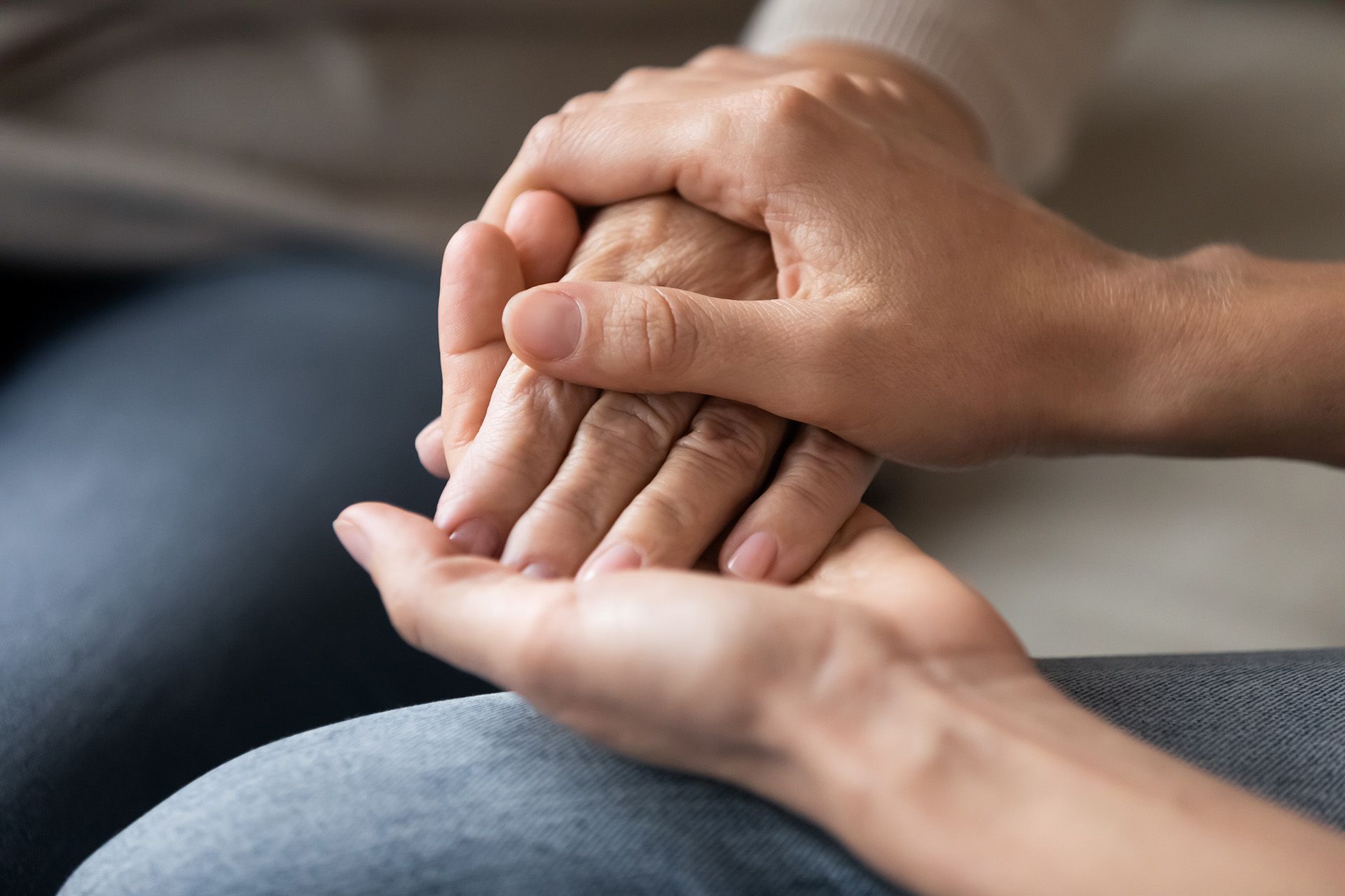 Two hands gently holding and comforting another hand on a lap