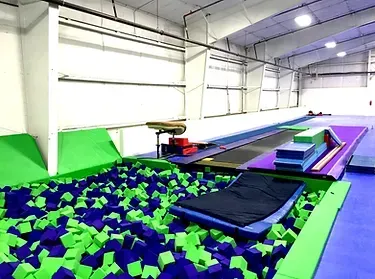 Indoor trampoline park with foam pit, trampolines, and padded ramps under bright lights