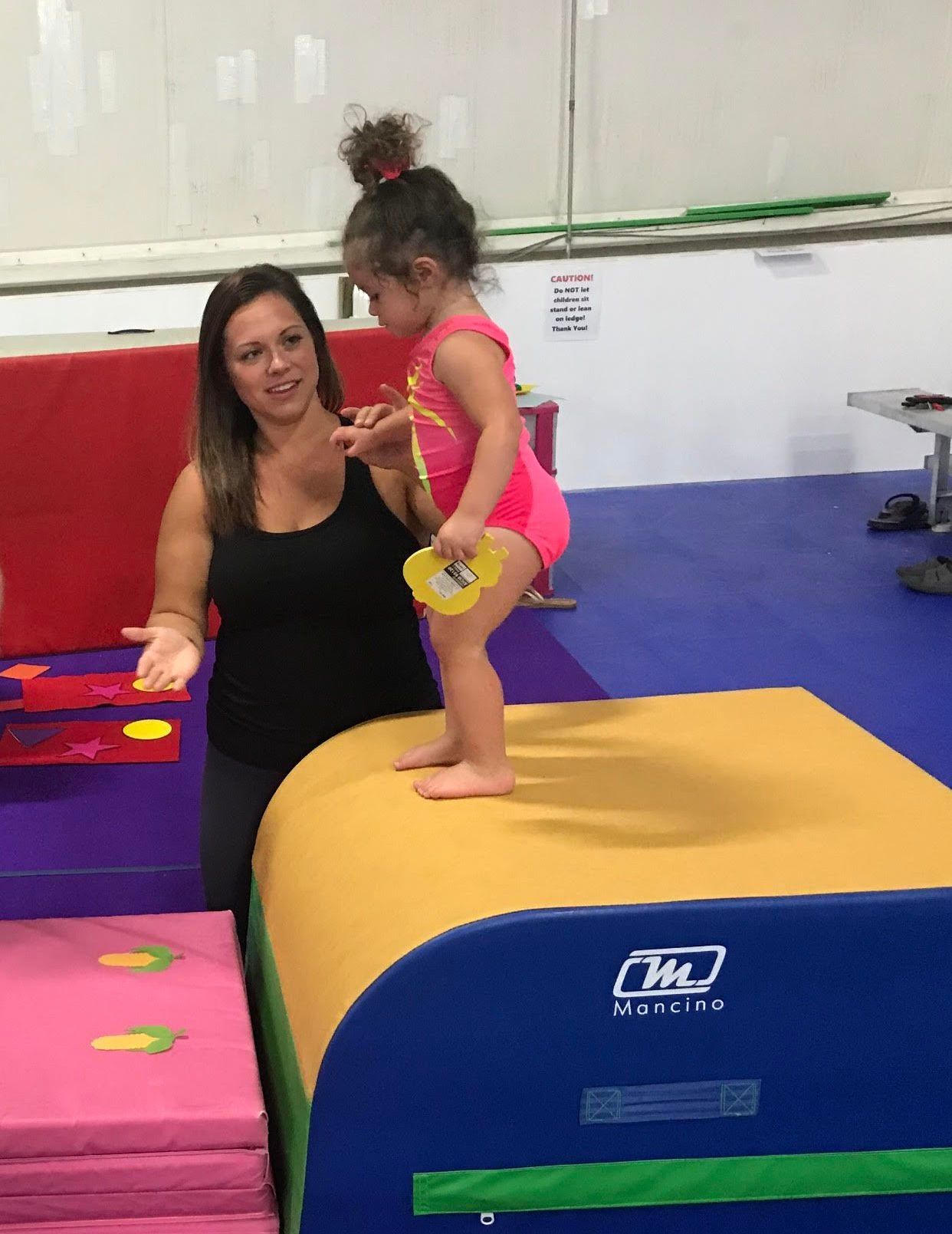 Adult spotting child on padded gym equipment in a playroom