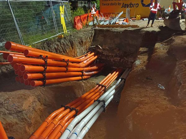 A bunch of orange pipes are stacked on top of each other in a trench.