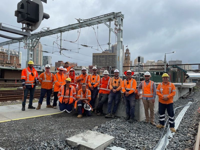 A group of construction workers are posing for a picture on a train track.