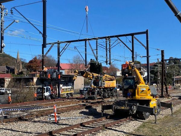 A yellow crane is lifting a metal structure on a train track.