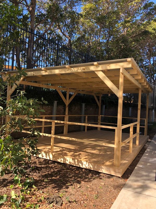 A wooden gazebo with a railing and a fence in the background.