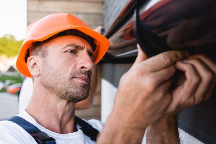 Worker in an orange hard hat inspecting a vehicle tire closely.