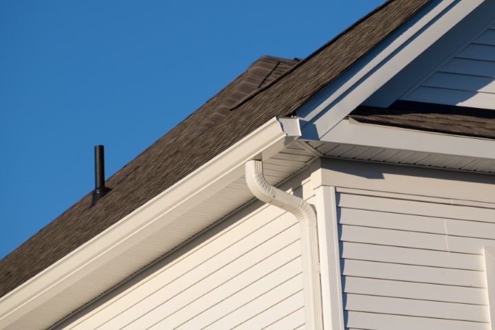 White house exterior with roof, gutter, and downspout against a blue sky
