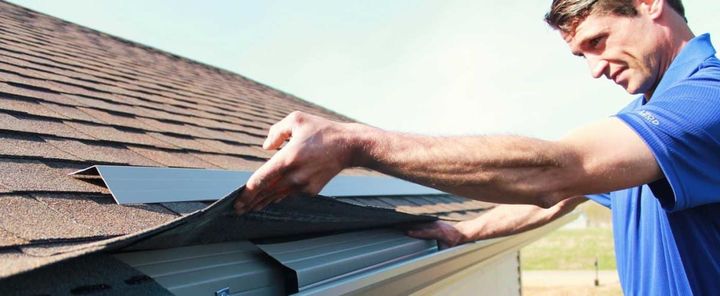 Worker installing a solar panel on a shingled rooftop with a screwdriver