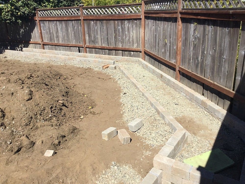 A backyard with a wooden fence and bricks in the dirt